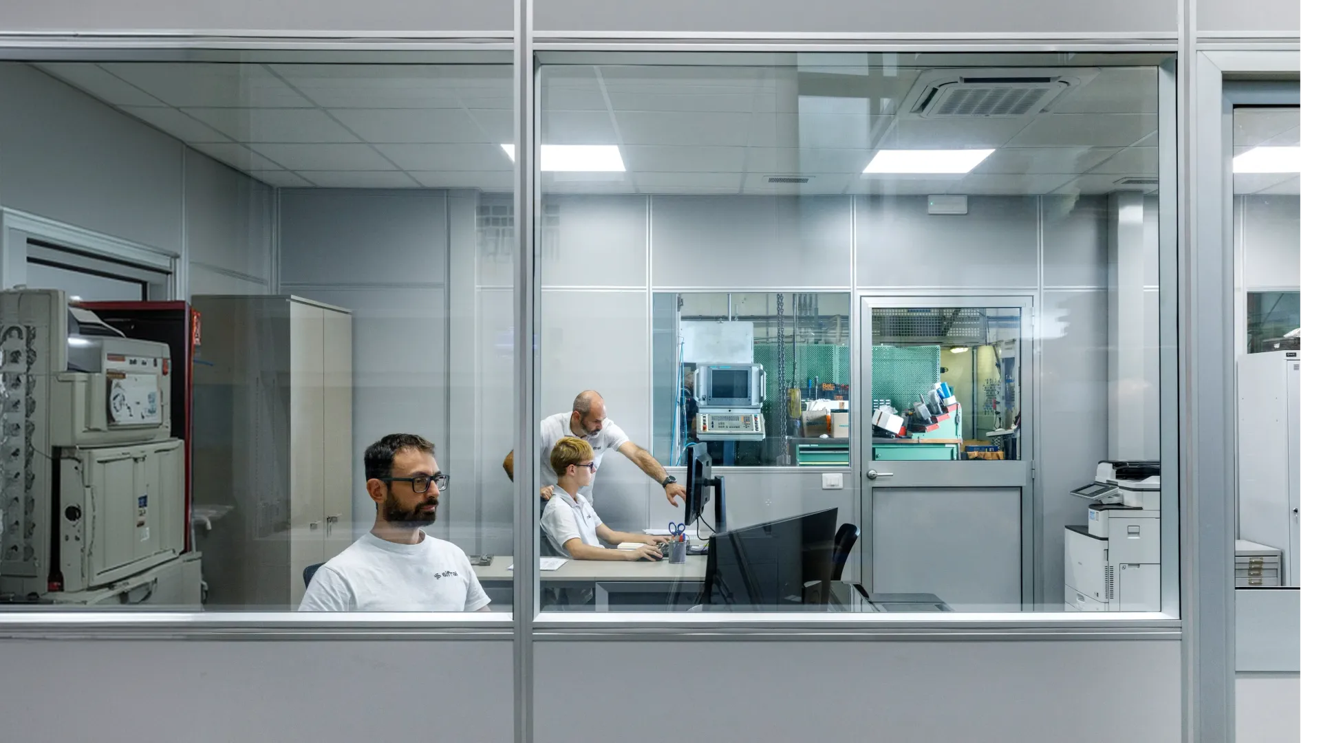 Techniciens au travail dans le bureau technique vitré de Sifral, donnant sur la production